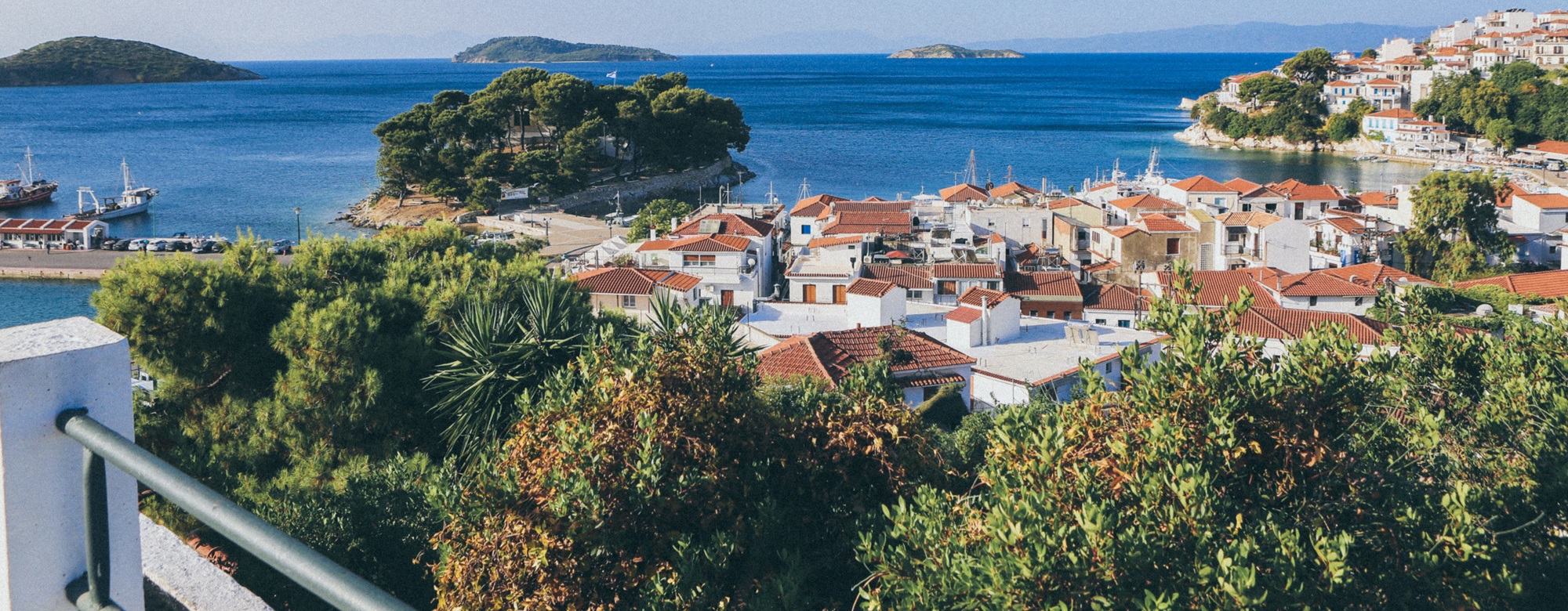 white and brown buildings near sea surrounded by trees and small islands in Skiathos, Greece